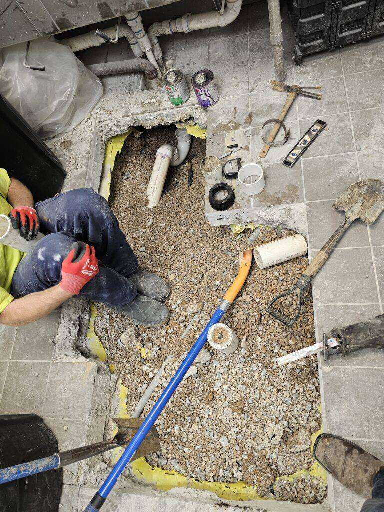 Open floor with exposed plumbing pipes and gravel during repair work