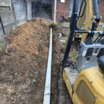 Excavation next to a building with exposed pipe in a trench