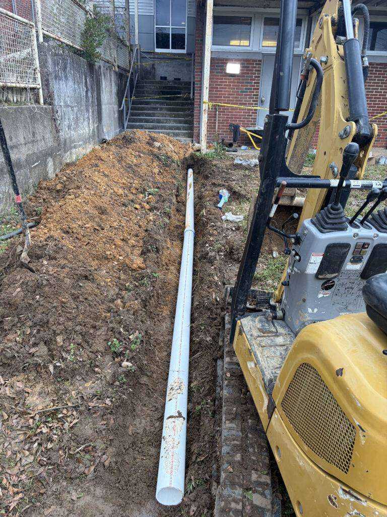 Excavation next to a building with exposed pipe in a trench
